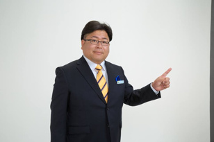 担当宅建士 大石浩之。看板とそろえたスーツ姿の上半身写真